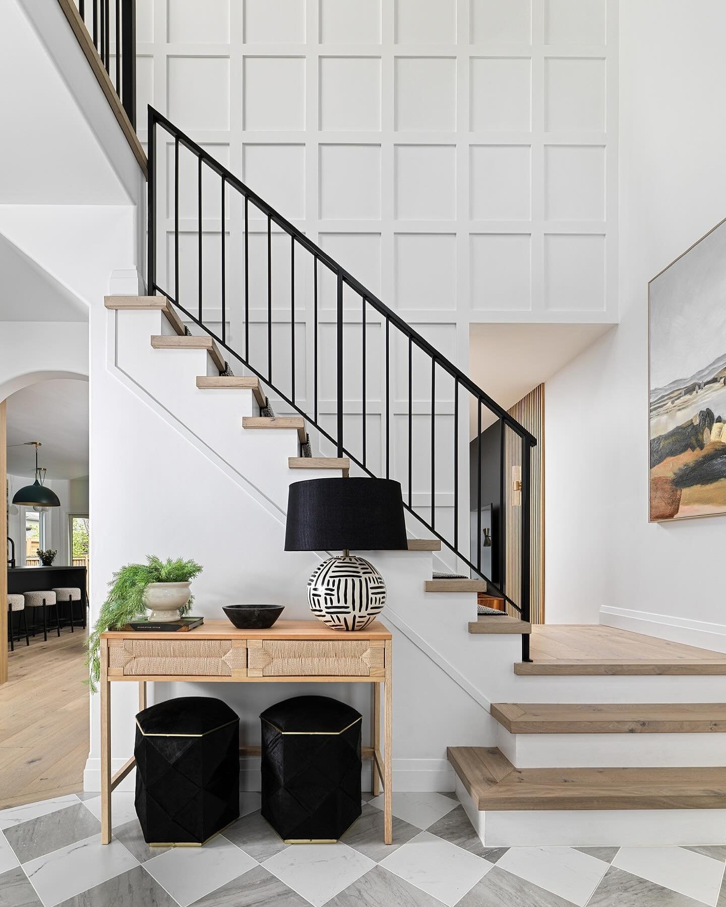 Modern white staircase featuring square board and batten wall paneling, black metal railing, and a styled console table entry.