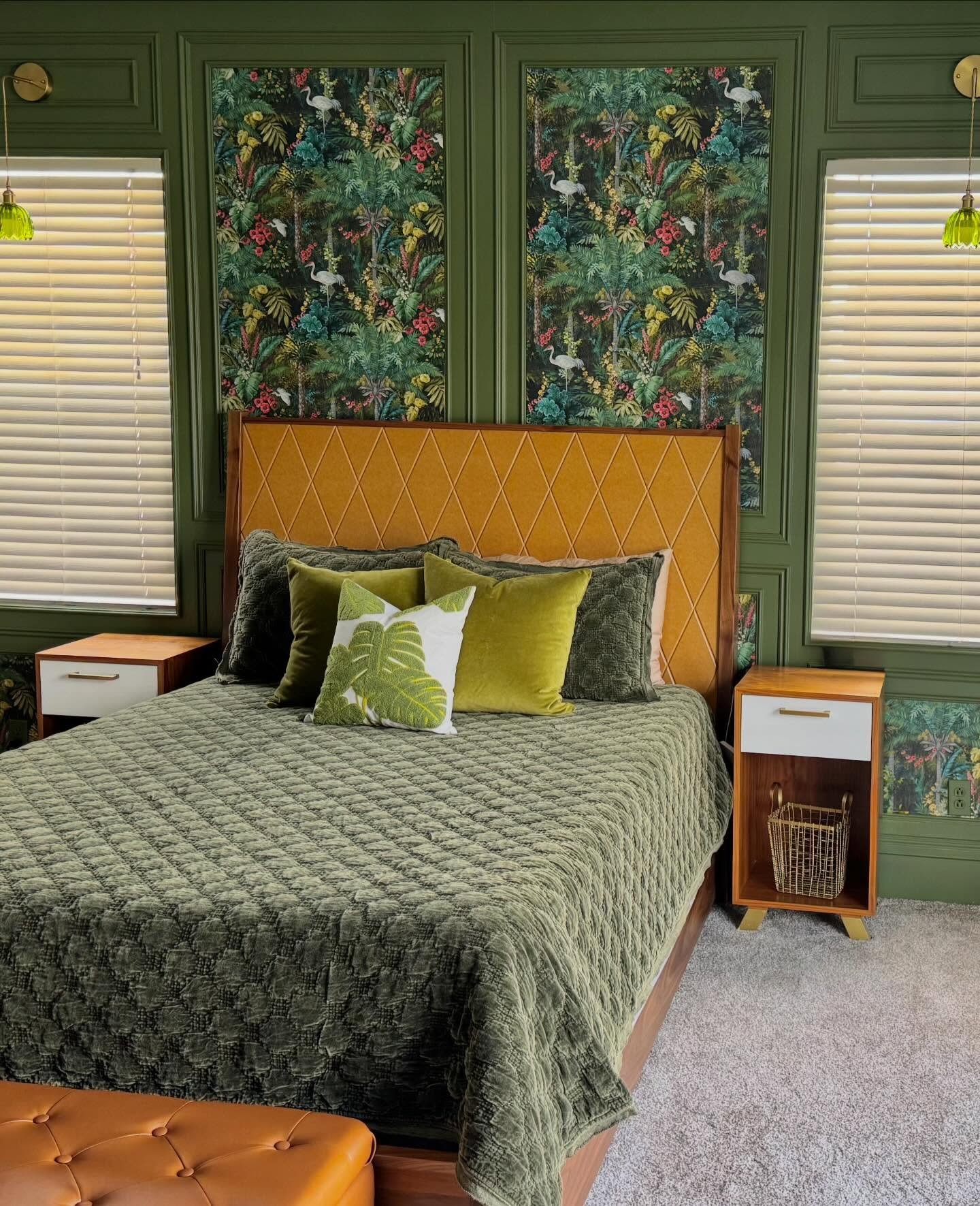 Bedroom accent wall featuring dark green molding framing tropical wallpaper panels behind a mustard headboard.