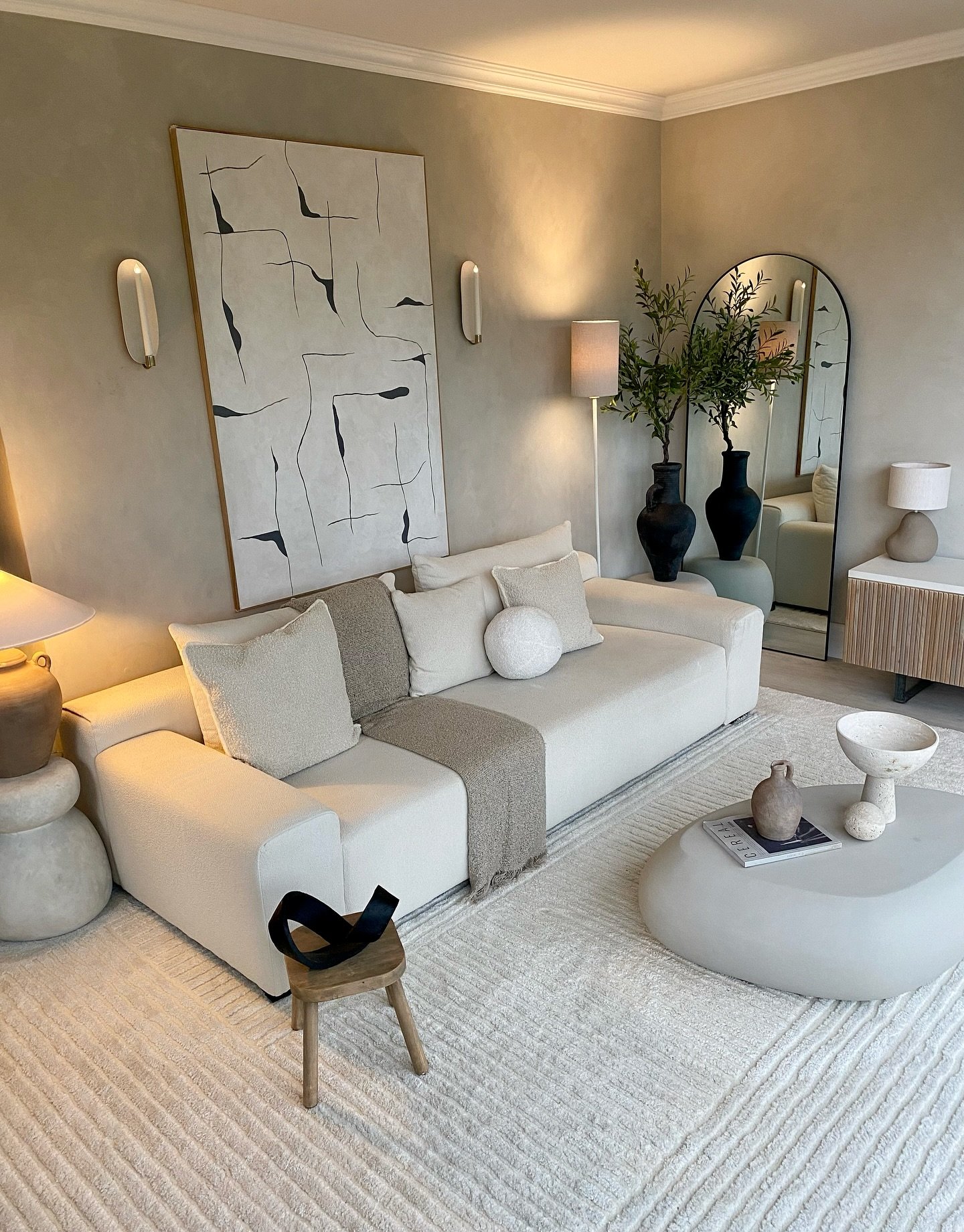 Large vertical abstract art print flanked by modern wall sconces above a cream sofa.