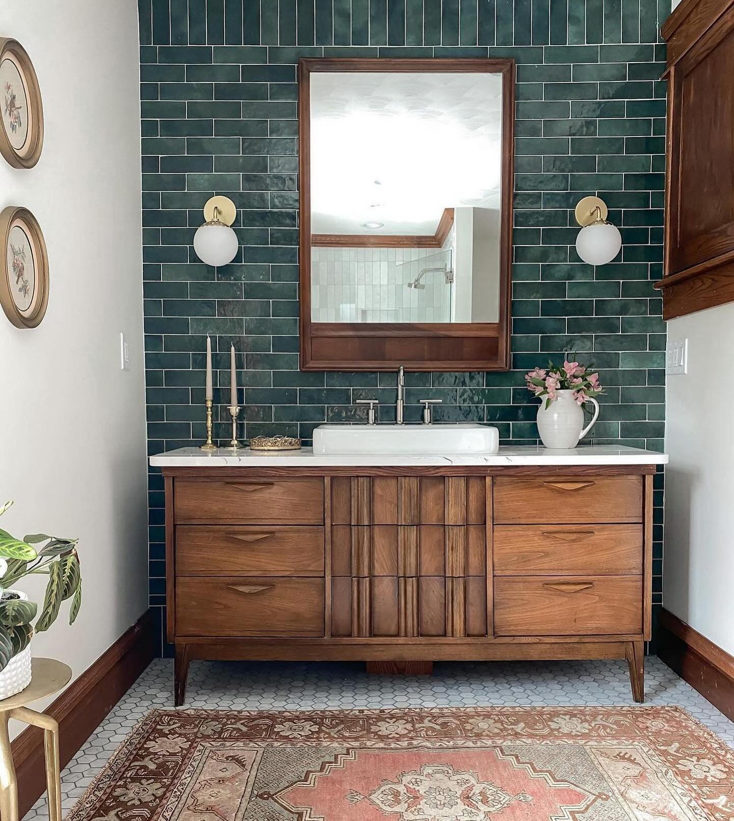Bathroom vanity featuring dark green subway tiles, a wooden mid-century cabinet, and a vintage rug.
