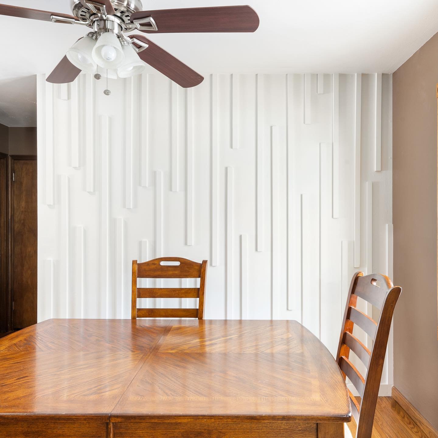 White dining room accent wall featuring random vertical wood slat molding and a wooden table.