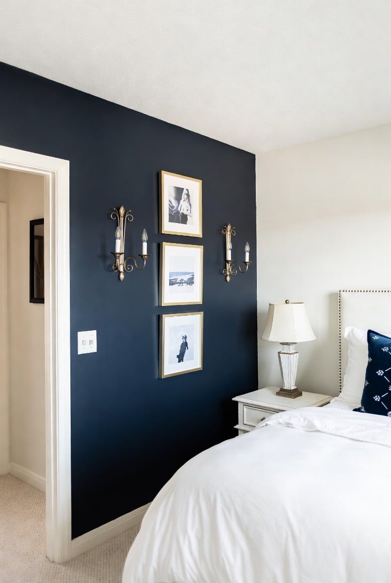 Navy blue accent wall featuring a vertical stack of gold-framed art and brass wall sconces