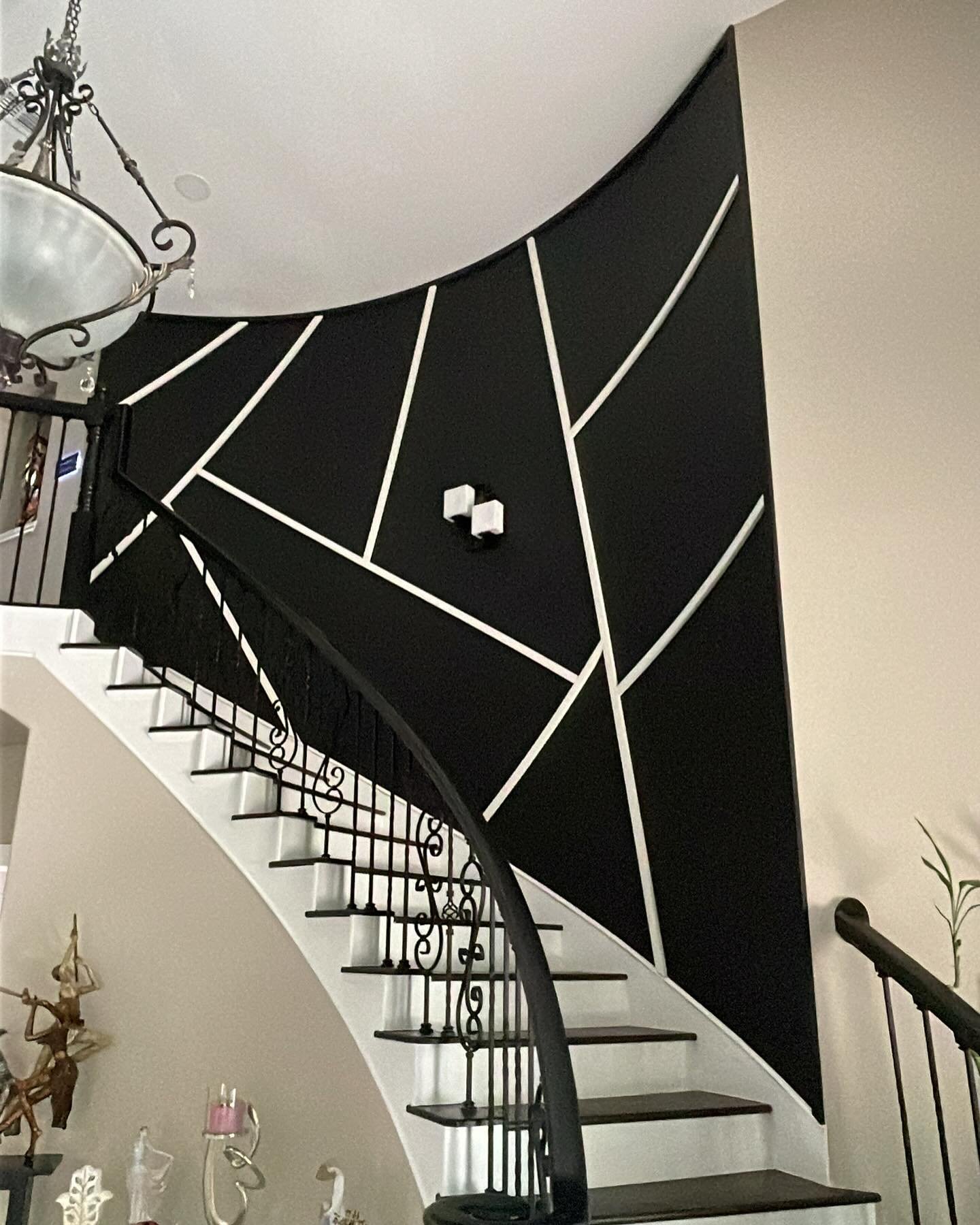 Curved staircase wall painted black with white geometric molding strips in an abstract pattern and small cube sconces.