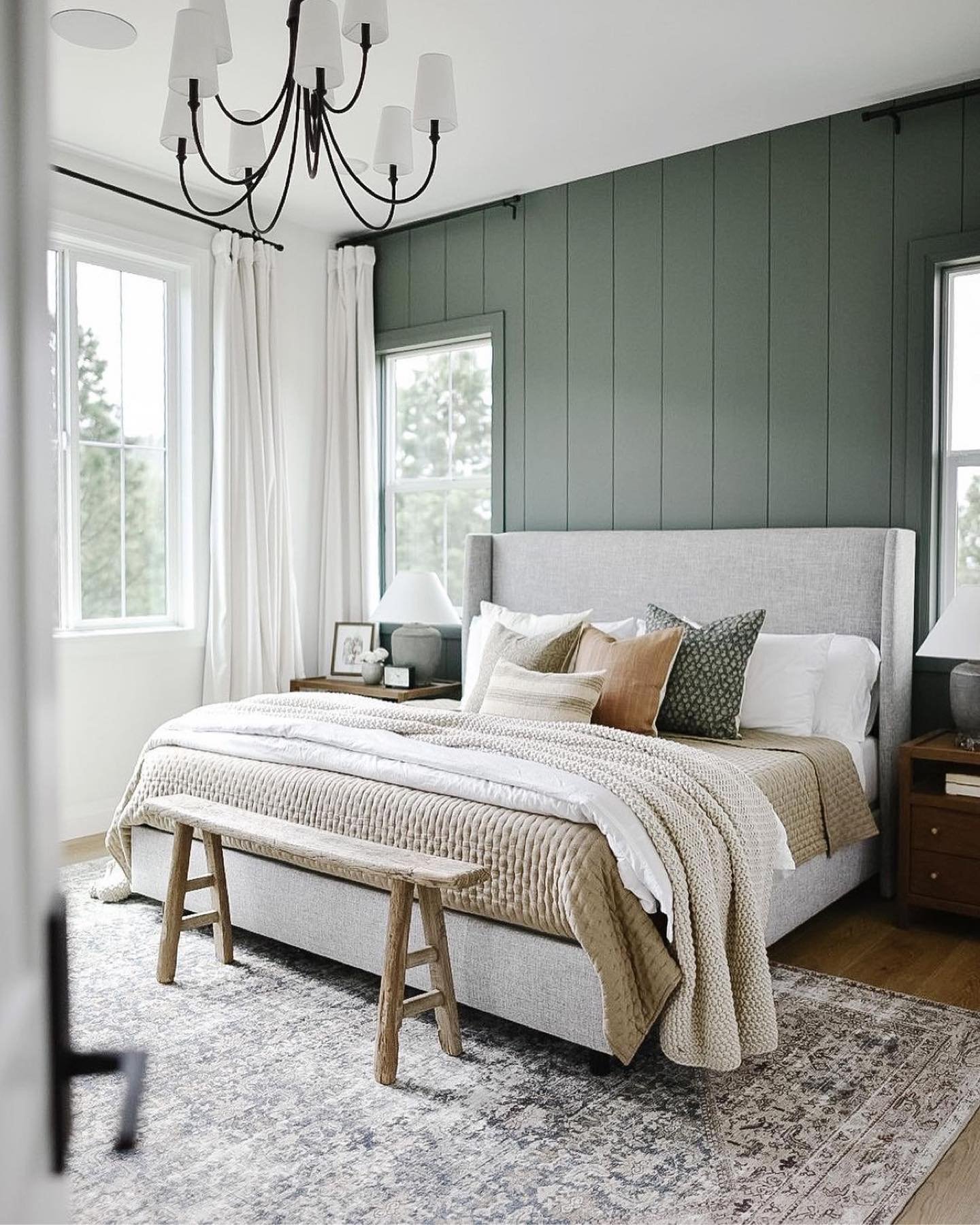 Bedroom featuring a dark sage green vertical plank accent wall behind a gray upholstered bed and rustic bench.