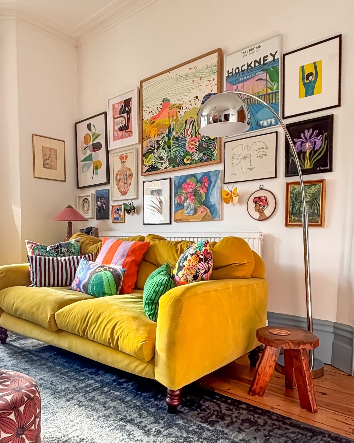 Vibrant floor-to-ceiling gallery wall with colorful eclectic art above a yellow velvet sofa.