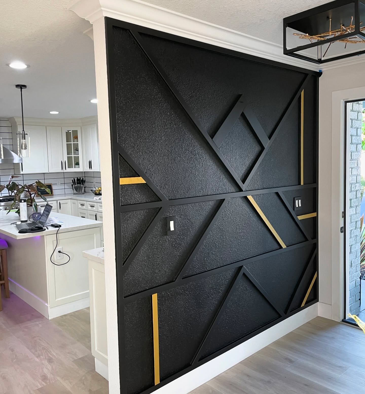Modern entryway room divider featuring black textured wall, geometric molding, and gold accents.