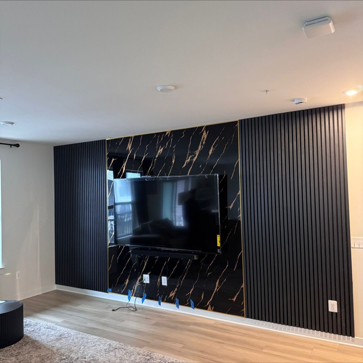 Black marble TV wall with gold veins and dark vertical slat siding.