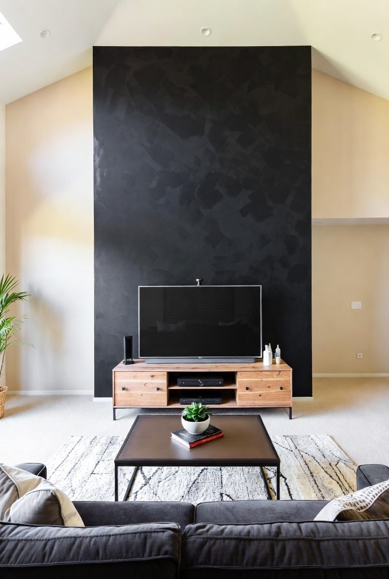 Living room with a high vaulted ceiling featuring a tall, textured black accent wall behind a television.