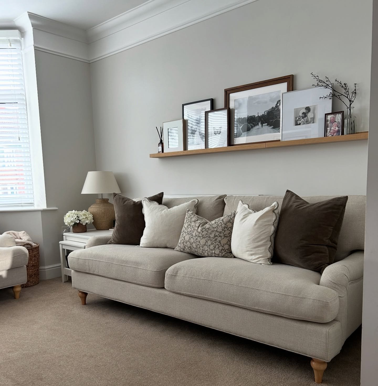 Wood picture ledge holding layered black and white photos above a beige sofa.