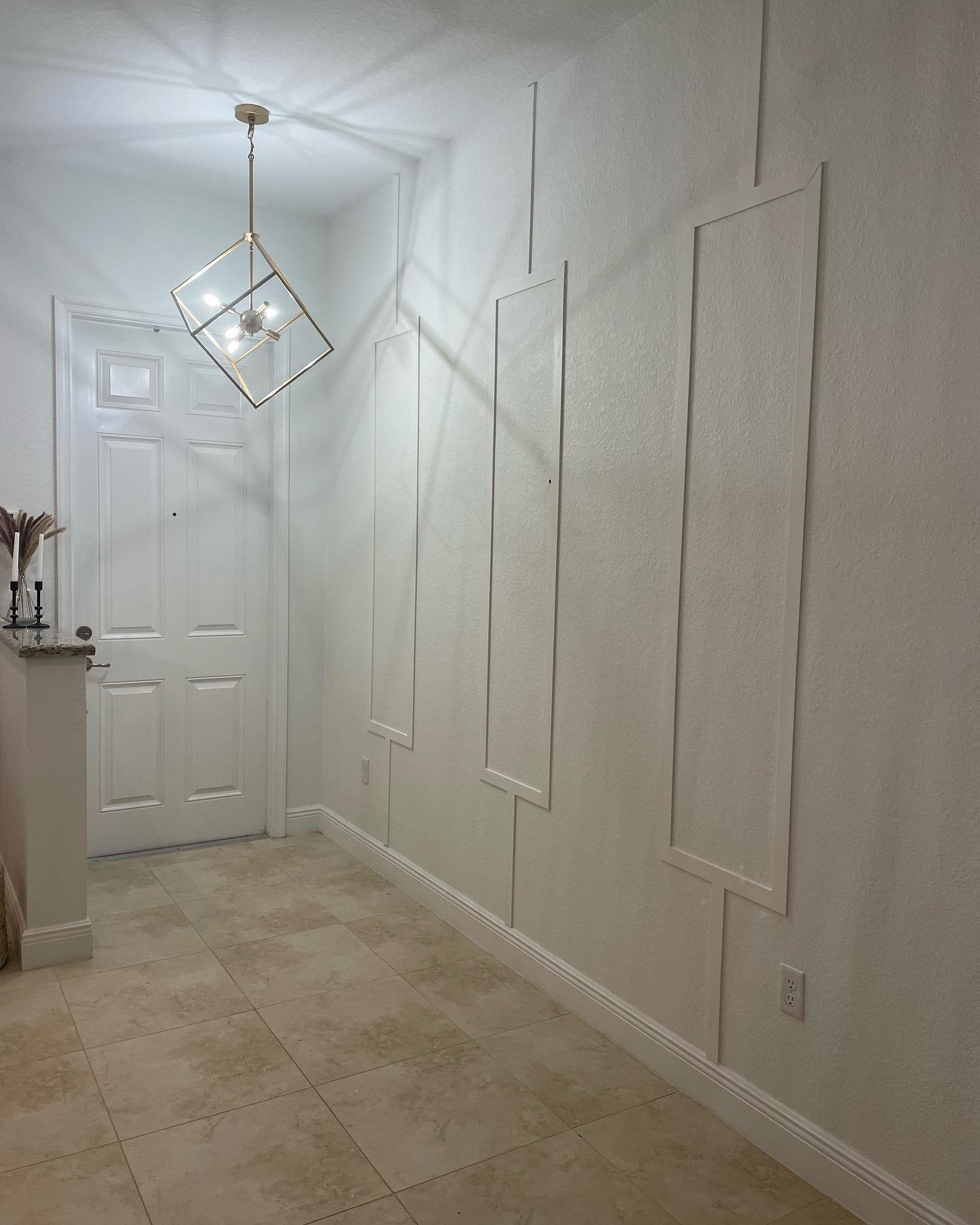 Hallway accent wall featuring white vertical rectangular molding, textured walls, and a gold geometric pendant light.