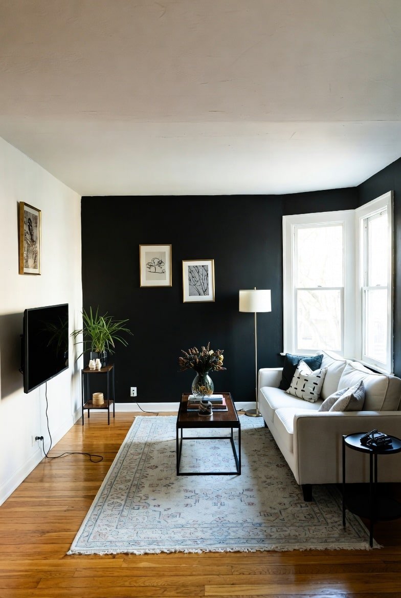 Living room featuring a matte Black Accent Wall with gold framed art, a white sofa, and a bay window.
