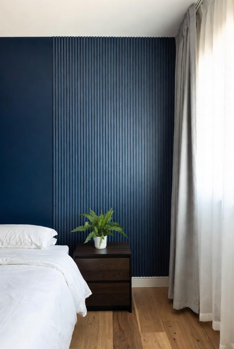 Navy blue accent wall with partial vertical fluted paneling behind dark wood nightstand