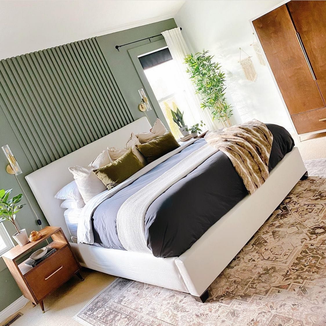 Bedroom with a sage green accent wall featuring narrow vertical slats behind a white upholstered bed.