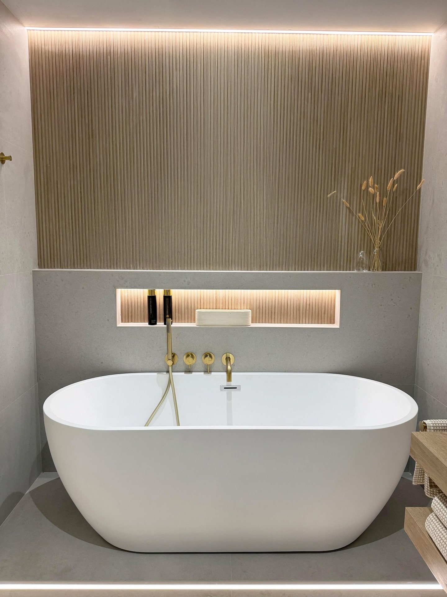 Modern bathroom featuring vertical wood slat accent wall with LED lighting behind a white tub.