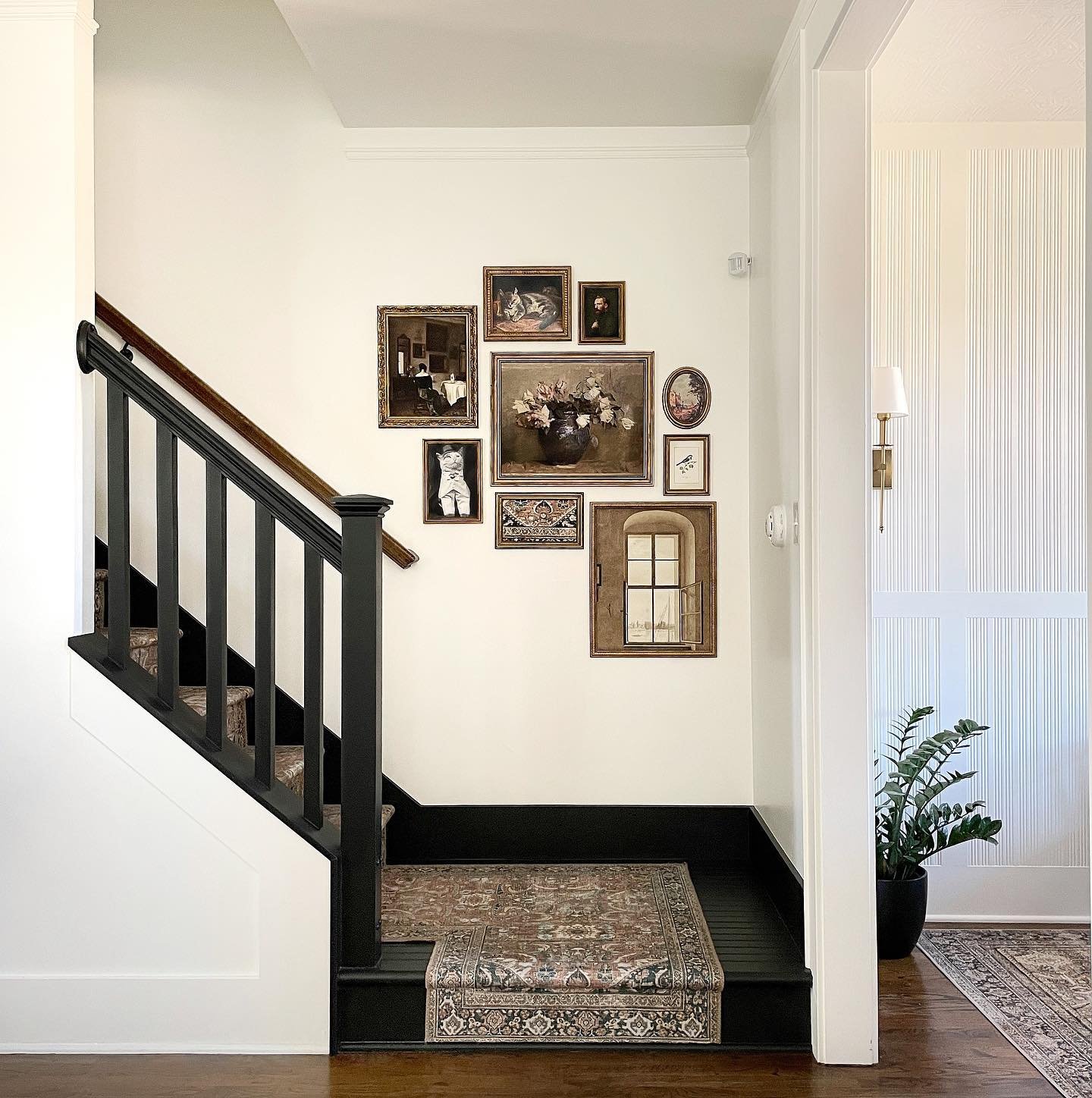 Staircase landing featuring a gallery wall of vintage oil paintings in gold frames next to a black railing.