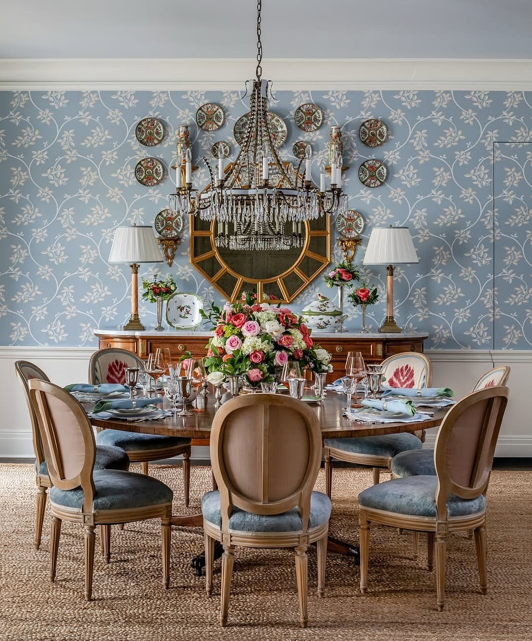 Traditional dining room featuring blue floral wallpaper, gold mirror, and wall-mounted plates