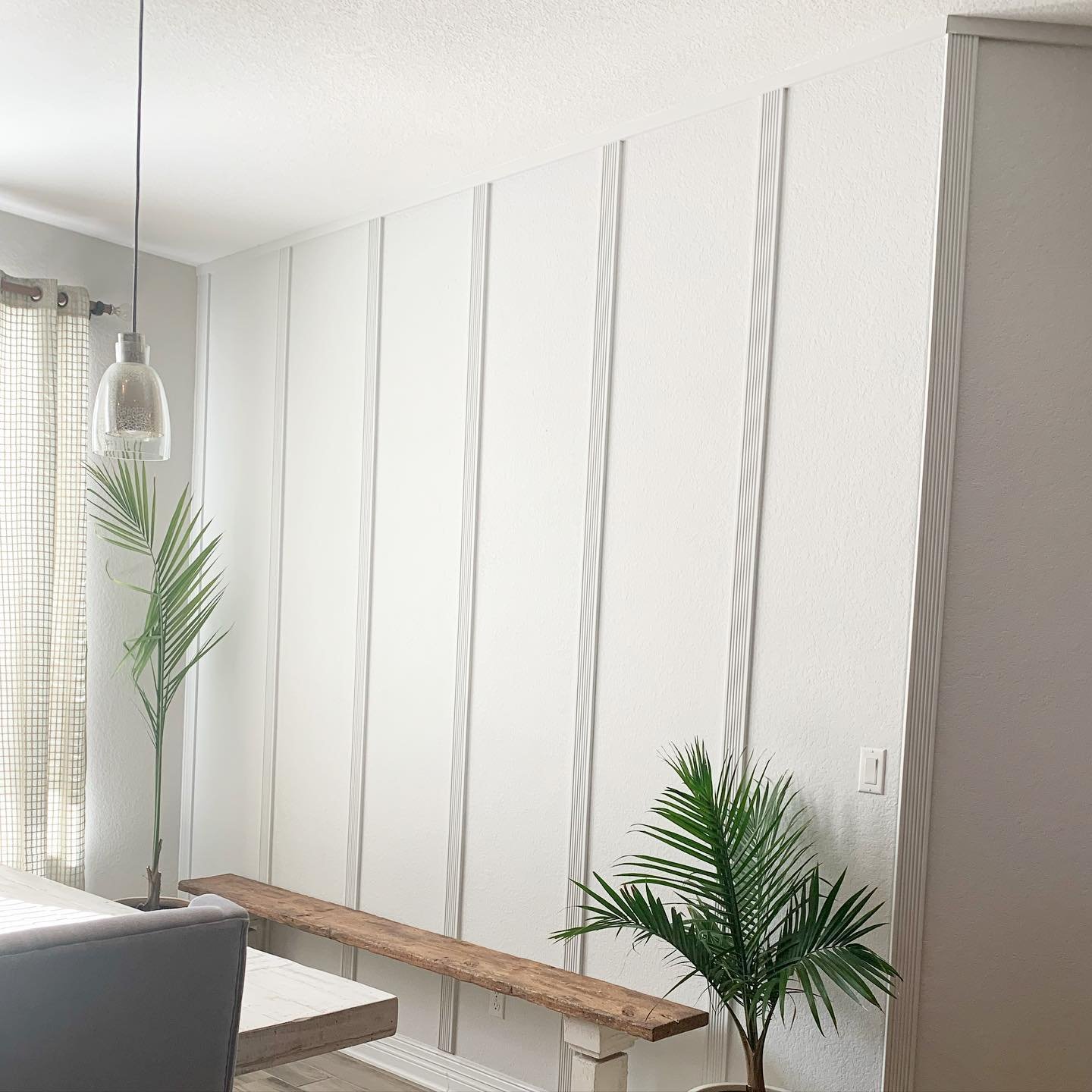 White dining room accent wall featuring vertical wood slats and a rustic wooden bench.