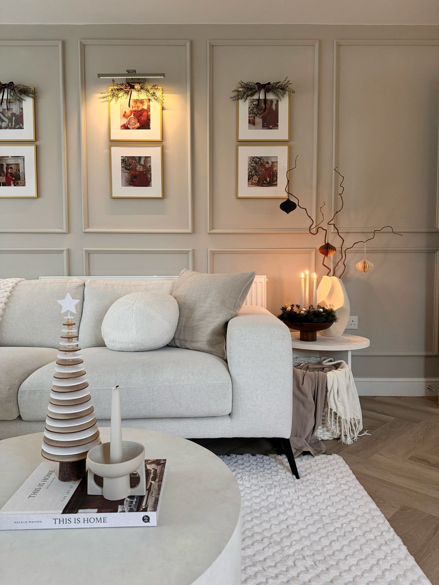 Vertical pairs of gold framed photos hanging within wall paneling above a beige sofa.