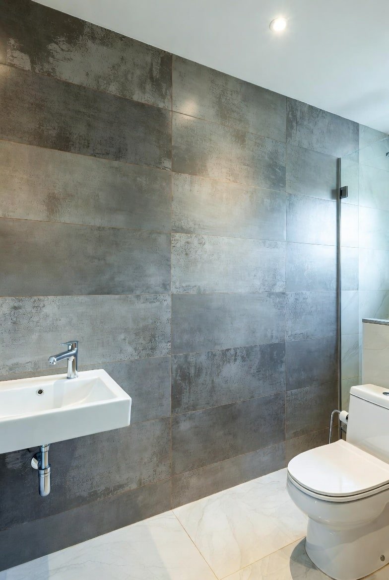 Modern bathroom featuring large format dark grey industrial tiles behind a white floating sink.