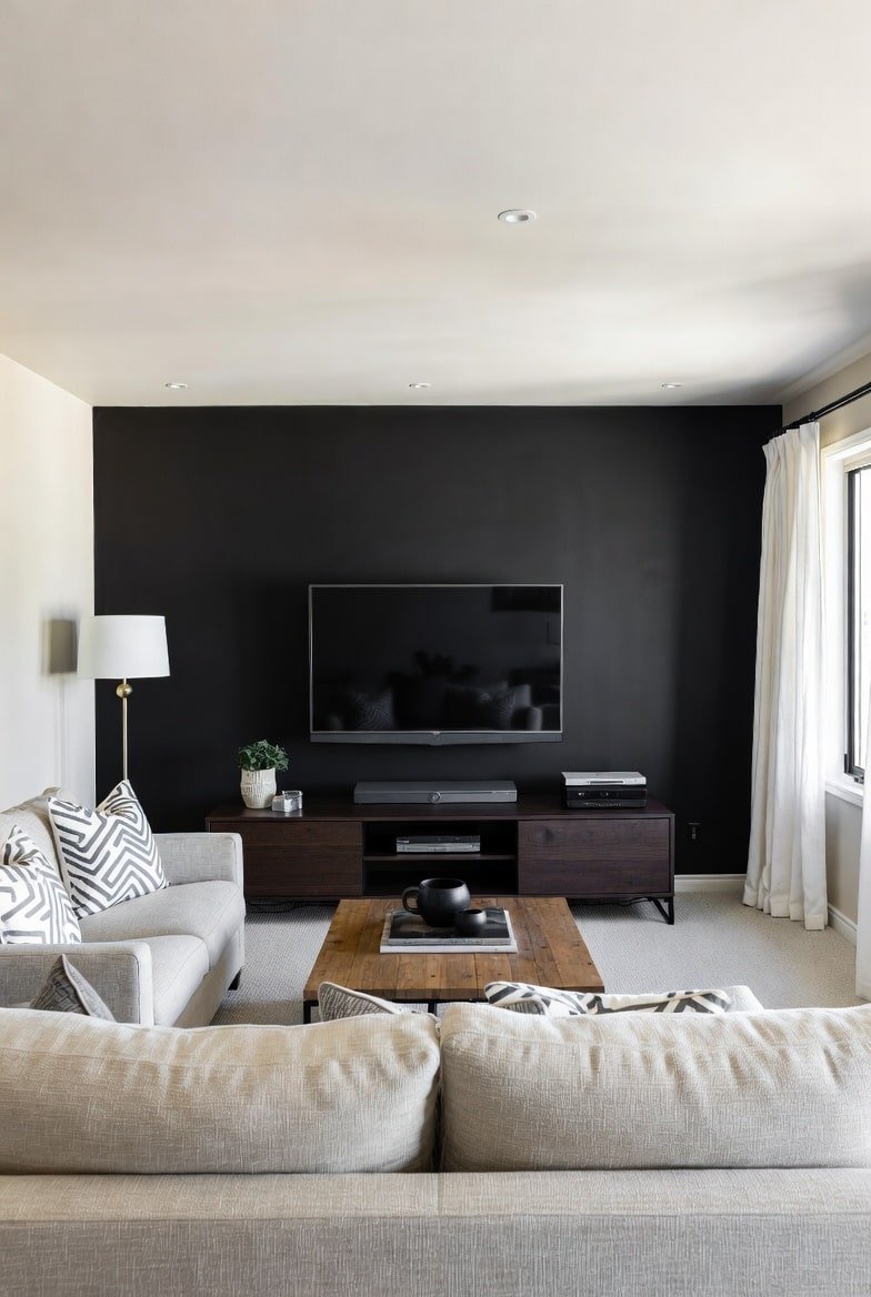 Living room featuring a matte Black Accent Wall, wooden coffee table, and light grey sectional sofa.