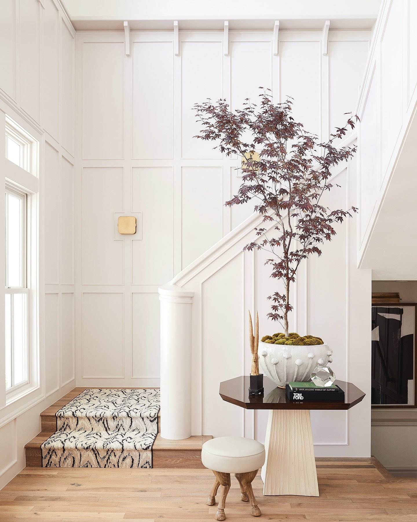 White staircase landing featuring floor-to-ceiling board and batten wall paneling, a large indoor tree in a pot, and a patterned runner.