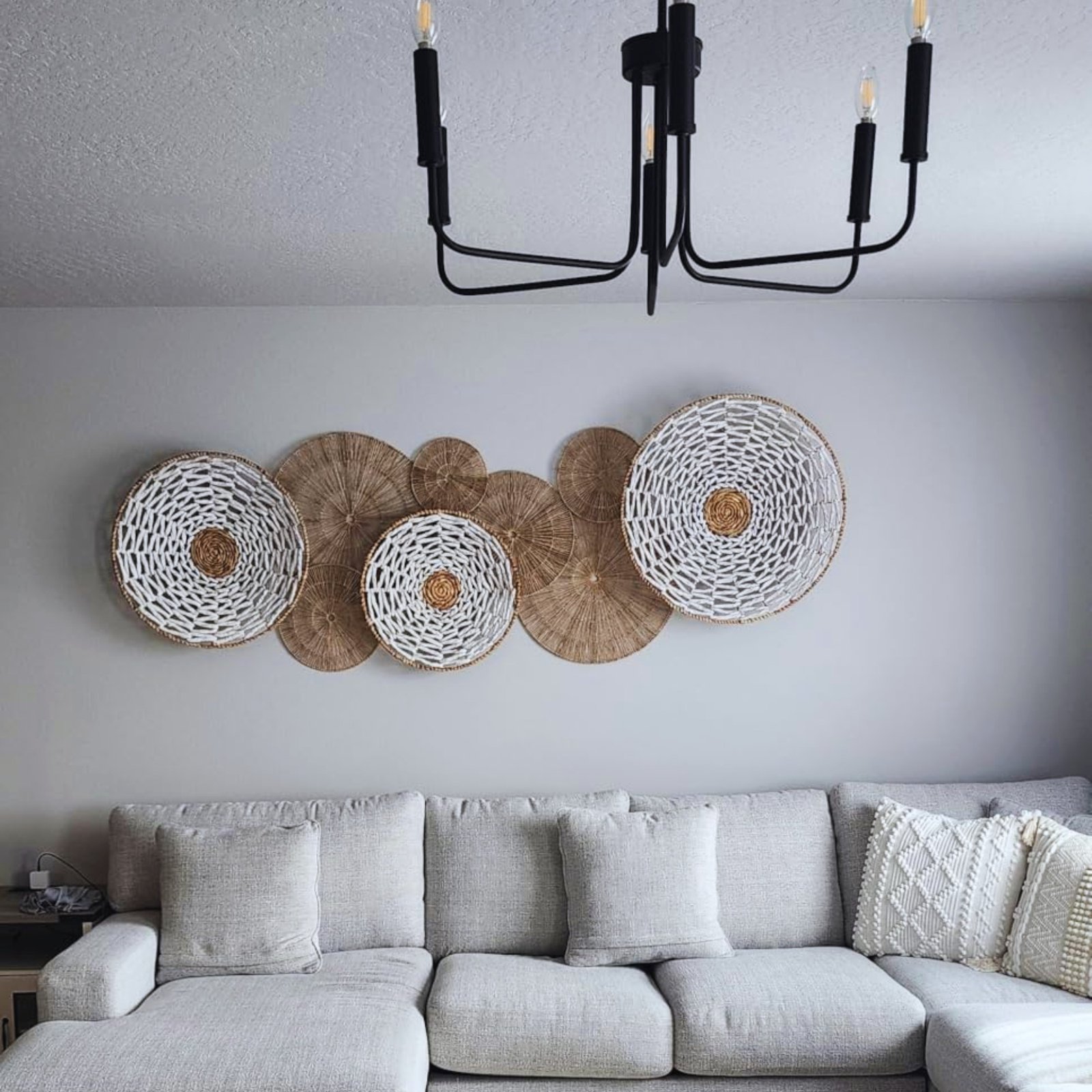 Collection of overlapping round woven baskets in natural and white tones hanging above a grey sectional sofa.