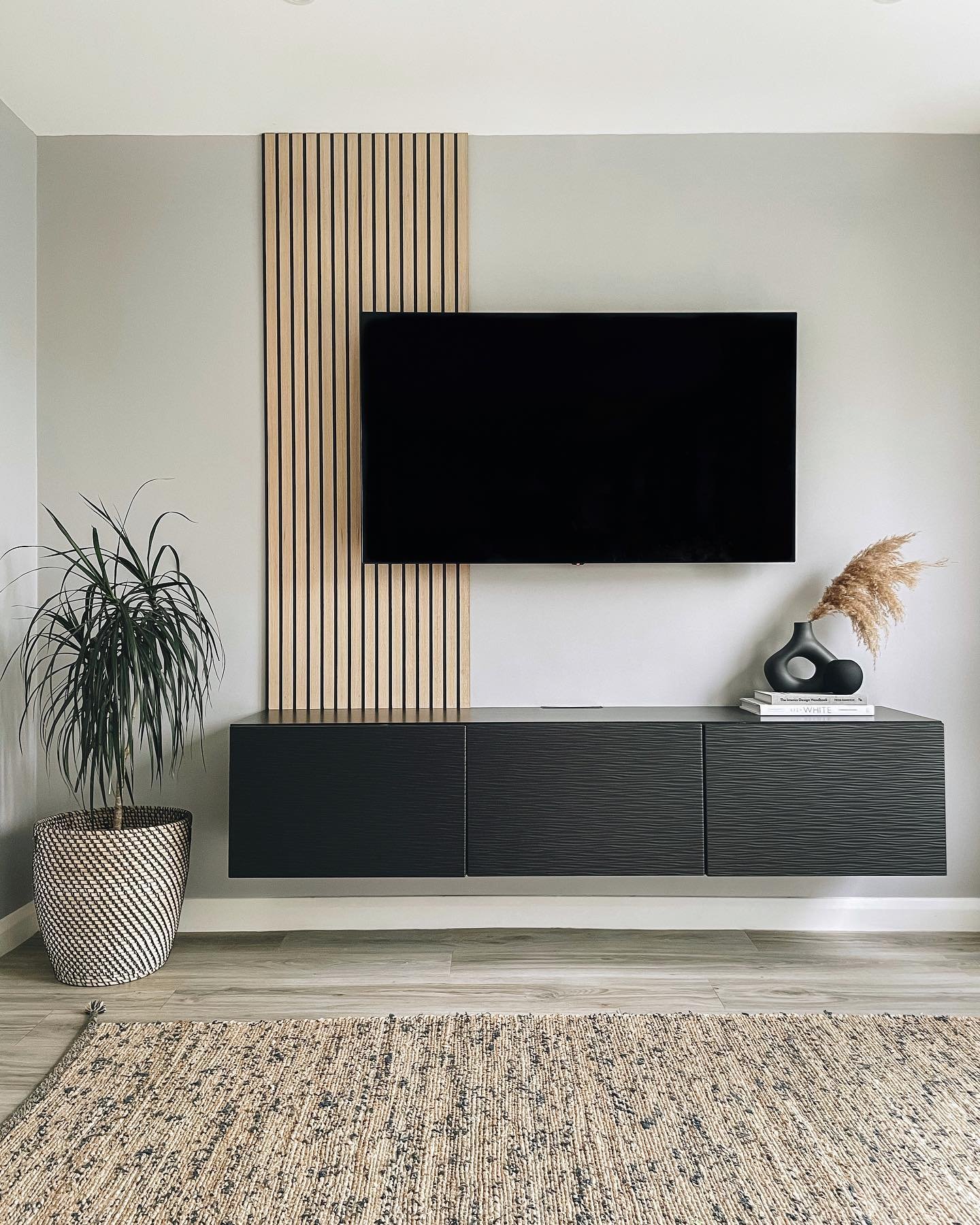 Grey wall with vertical wood slat strip behind TV and black floating console.
