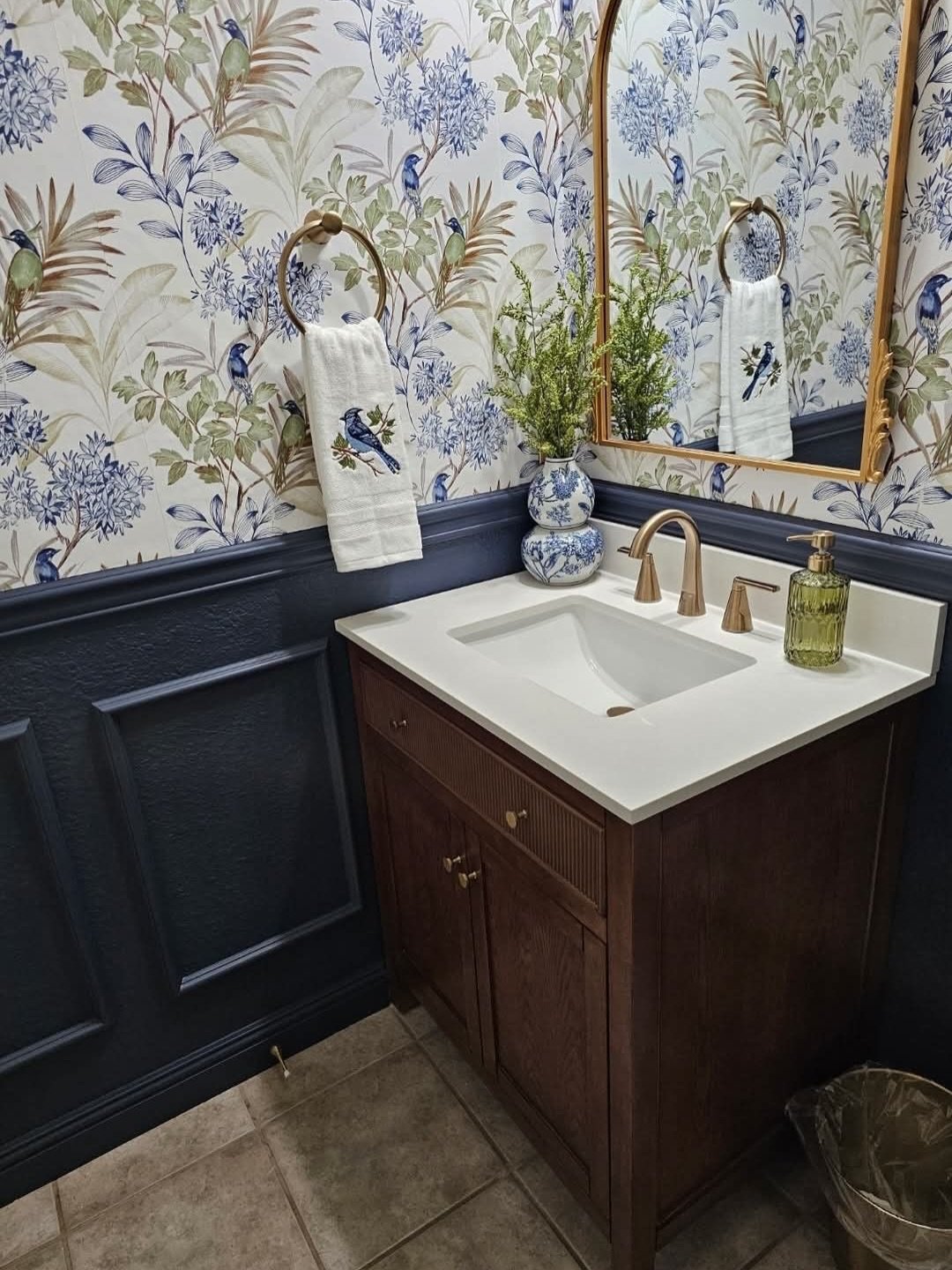 Bathroom wall decor featuring navy blue wainscoting and bird wallpaper behind wood vanity