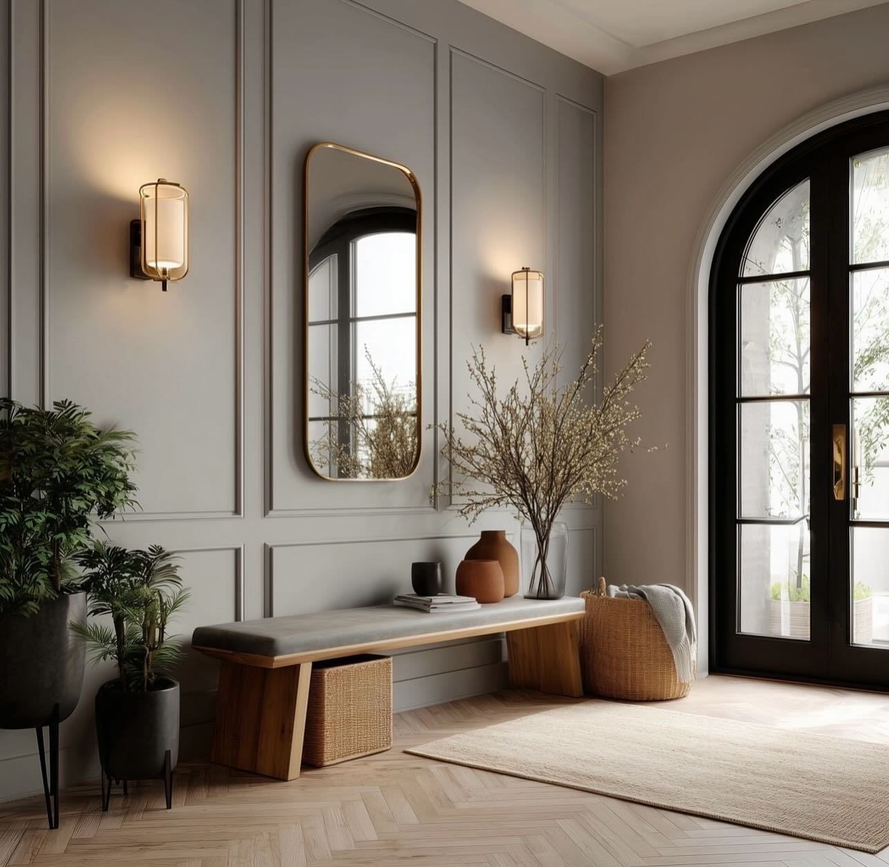 A grey paneled hallway wall features a brass mirror and sconces above a wooden bench near an arched glass door.