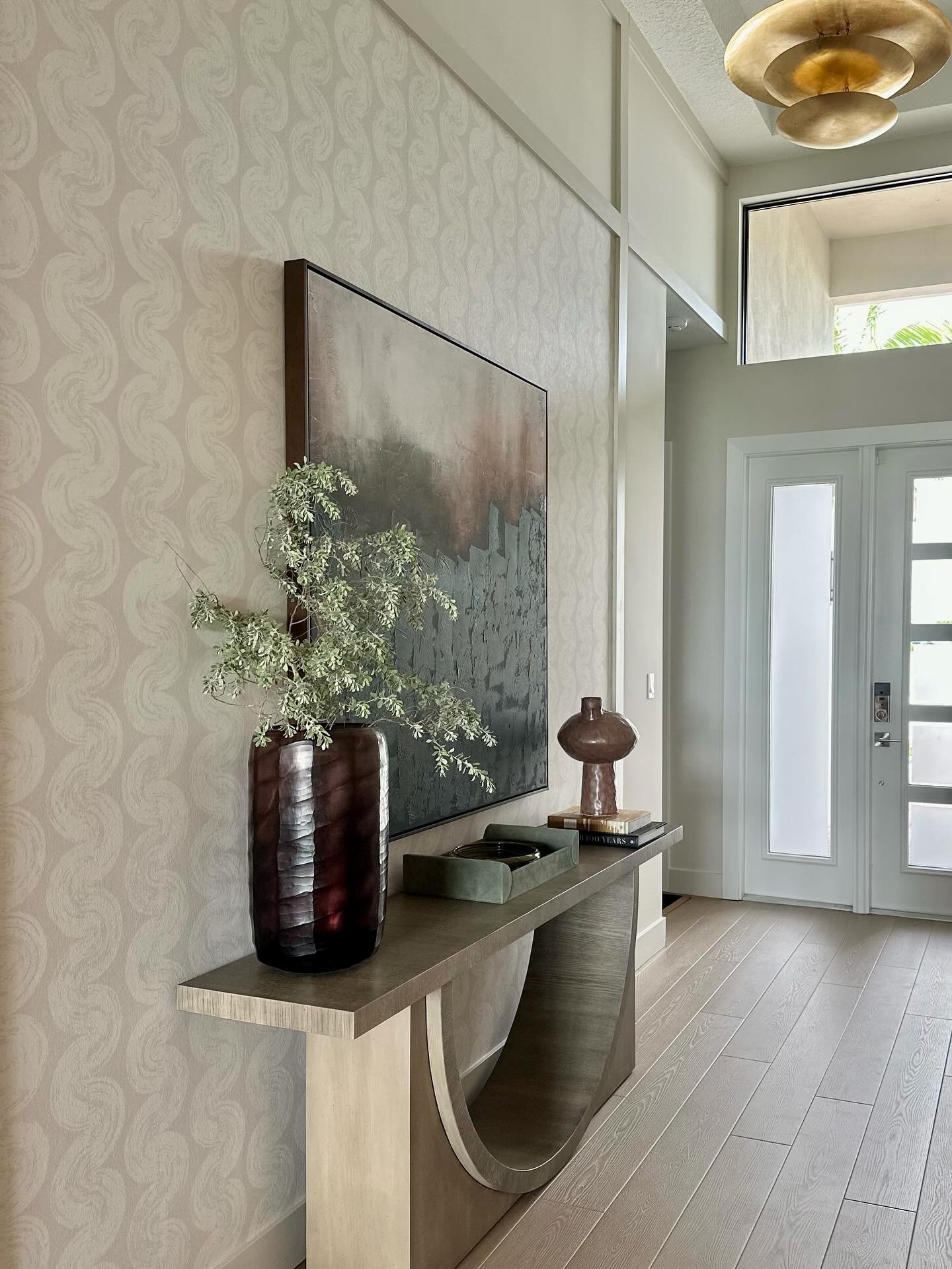 Bright entryway featuring beige wave pattern wallpaper, large abstract art, and a sculptural wood console table.