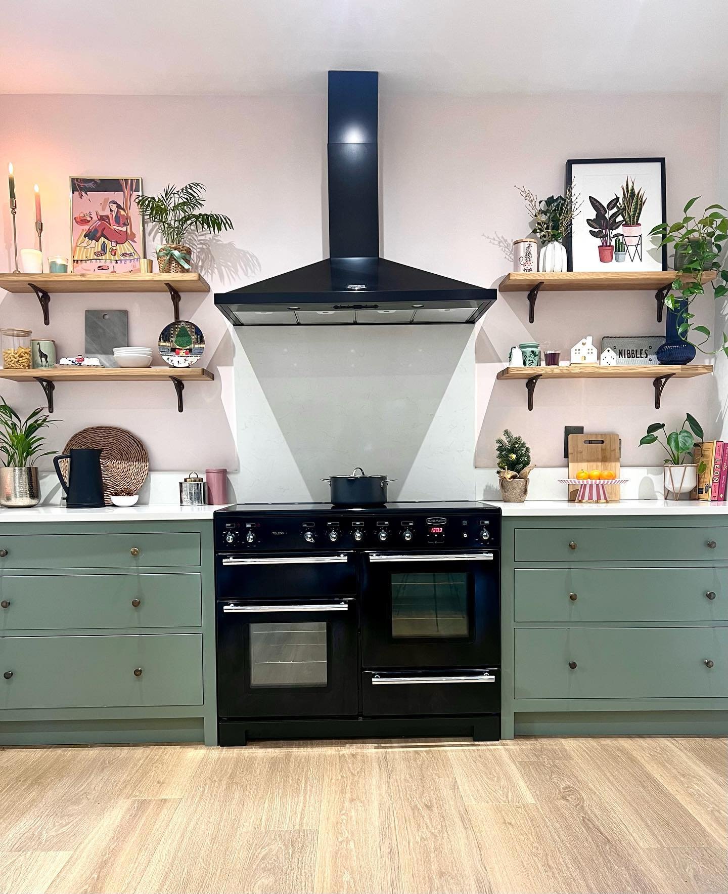 Kitchen featuring pale pink walls, green cabinets, black range cooker, and symmetrical open shelving