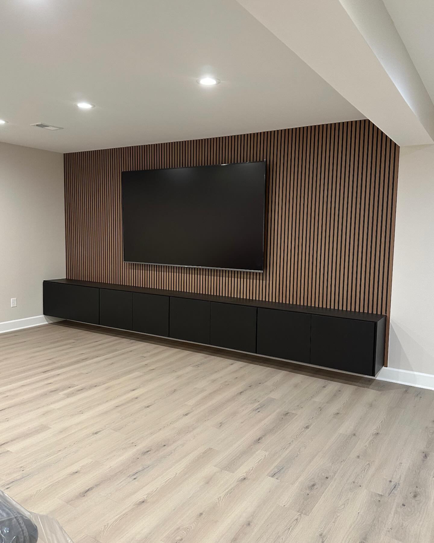 Wide vertical wood slat TV wall with long black floating media cabinet.