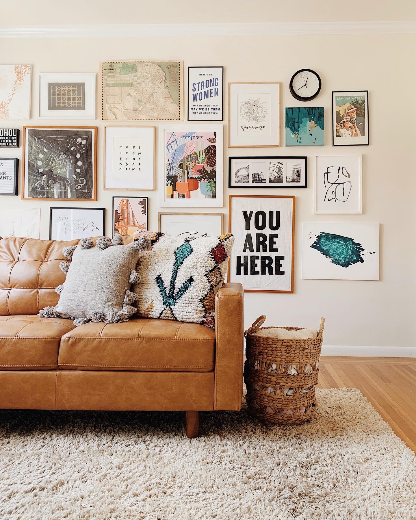 Large gallery wall featuring maps, typography art, and mixed frames above a tan leather sofa.