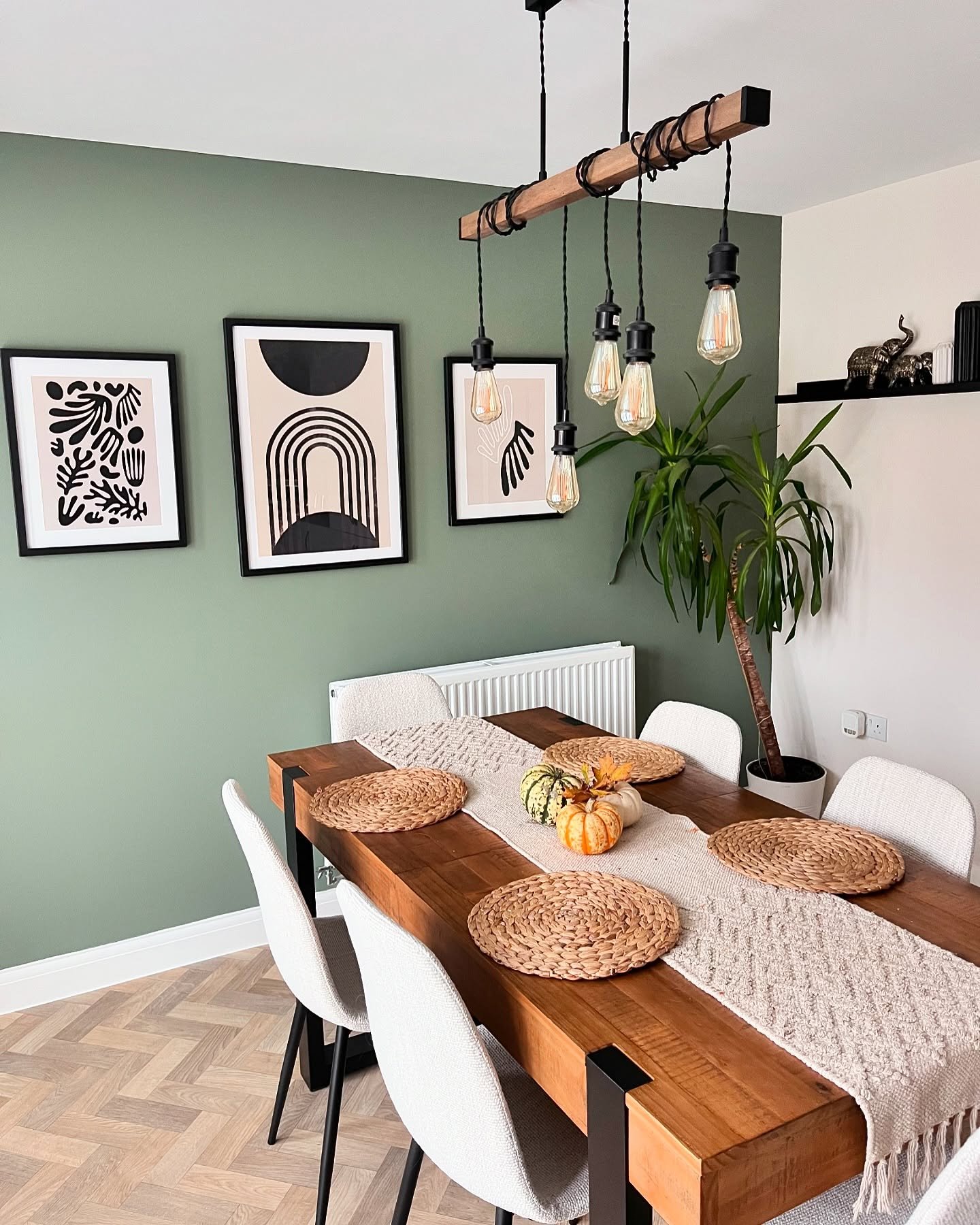 Dining room with sage green accent wall featuring three black and white abstract prints