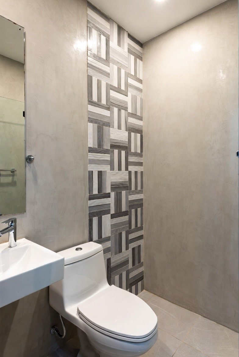Small bathroom with concrete walls and a vertical strip of basketweave tiles behind the toilet.