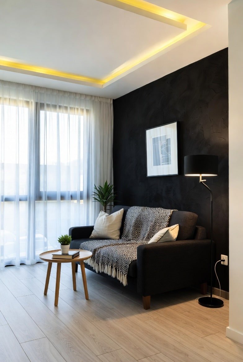 Living room featuring a textured plaster black accent wall with warm cove ceiling lighting and a dark grey sofa.