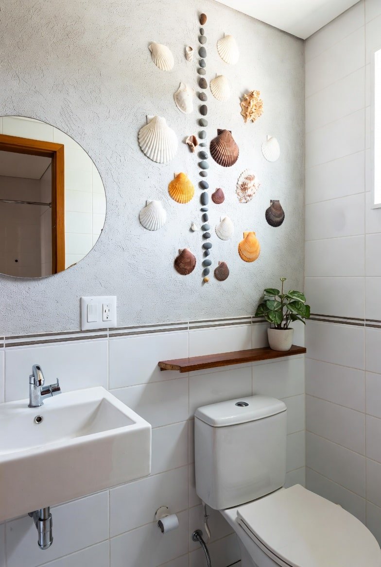 Bathroom wall decor featuring large seashells and stones arranged on textured grey wall