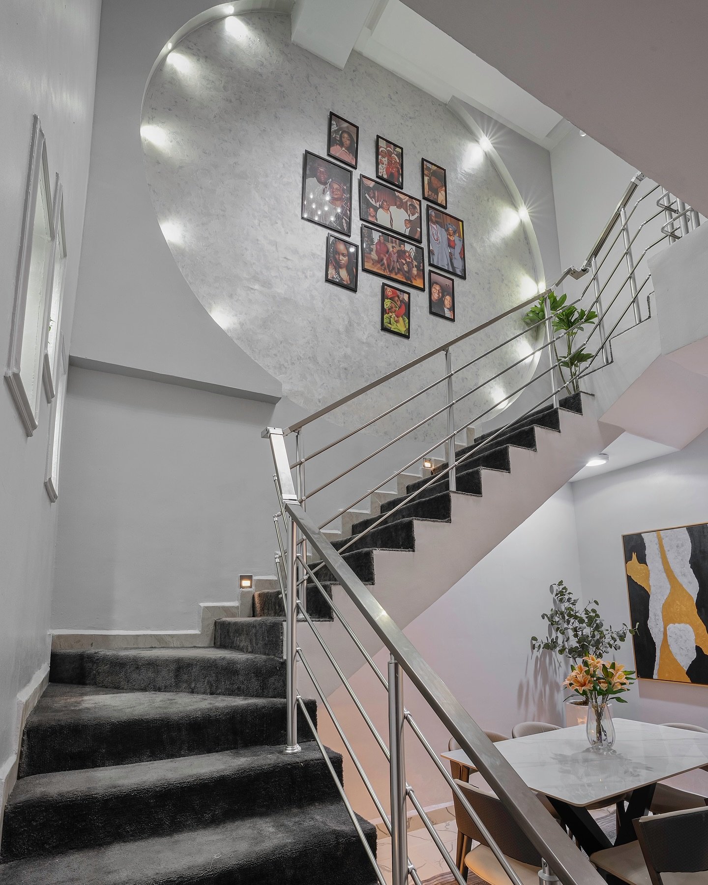 Modern staircase wall featuring a large circular recessed niche with built-in lighting containing a gallery of family photos.