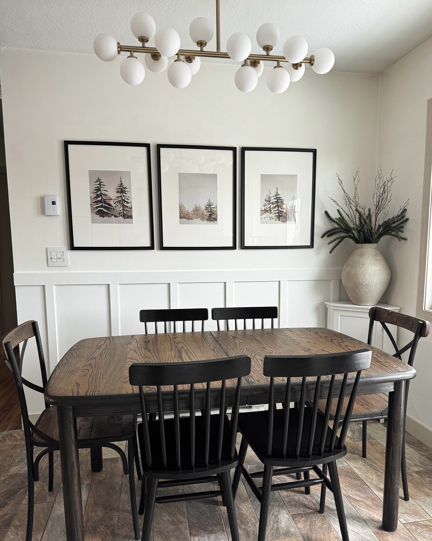 Dining room with white board and batten wall featuring three pine tree prints and black farmhouse chairs