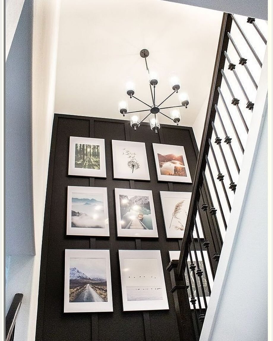 Staircase featuring a black board and batten accent wall with a grid of white-framed nature prints and a modern chandelier.