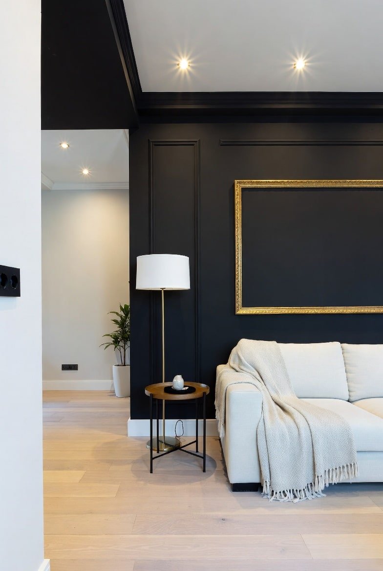 Living room featuring a paneled Black Accent Wall with a large gold empty frame and cream sofa.