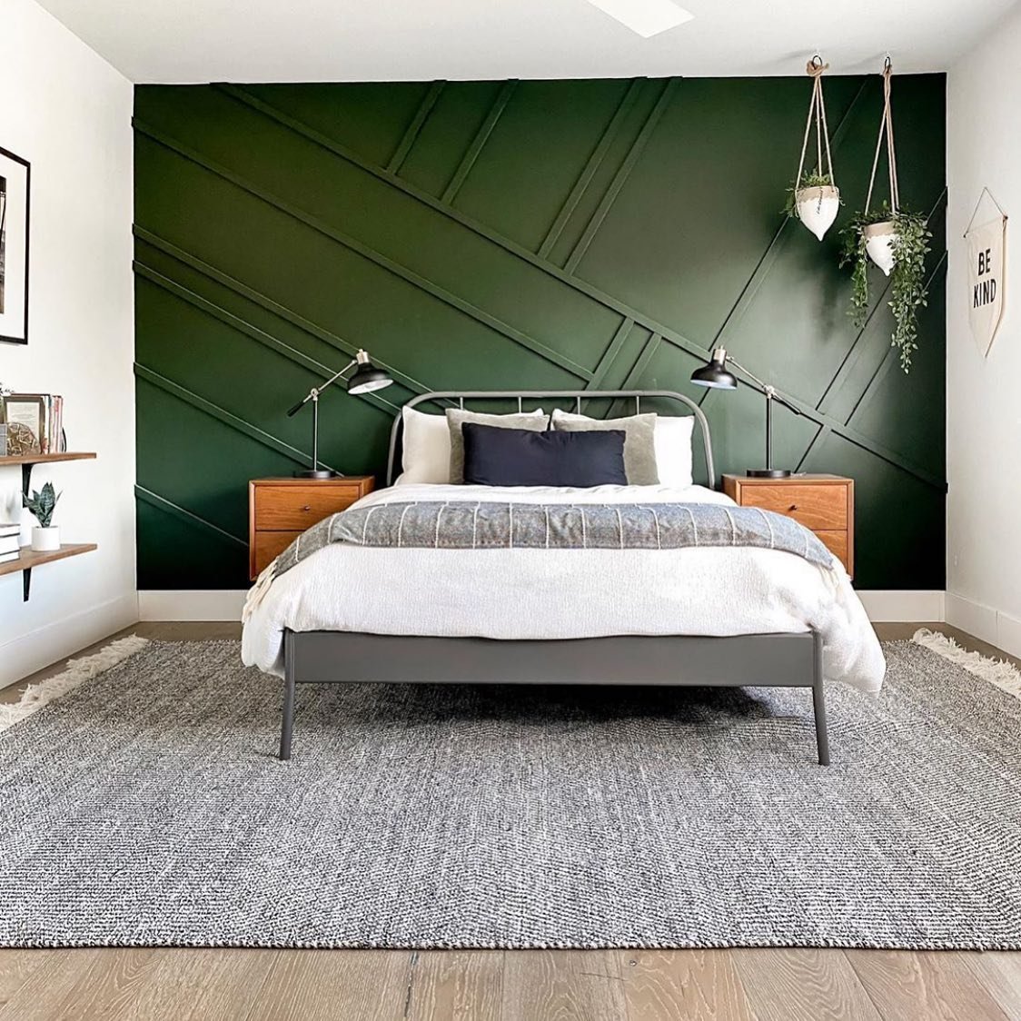 Bedroom with a dark green accent wall featuring asymmetric diagonal wood slats behind a grey metal bed.