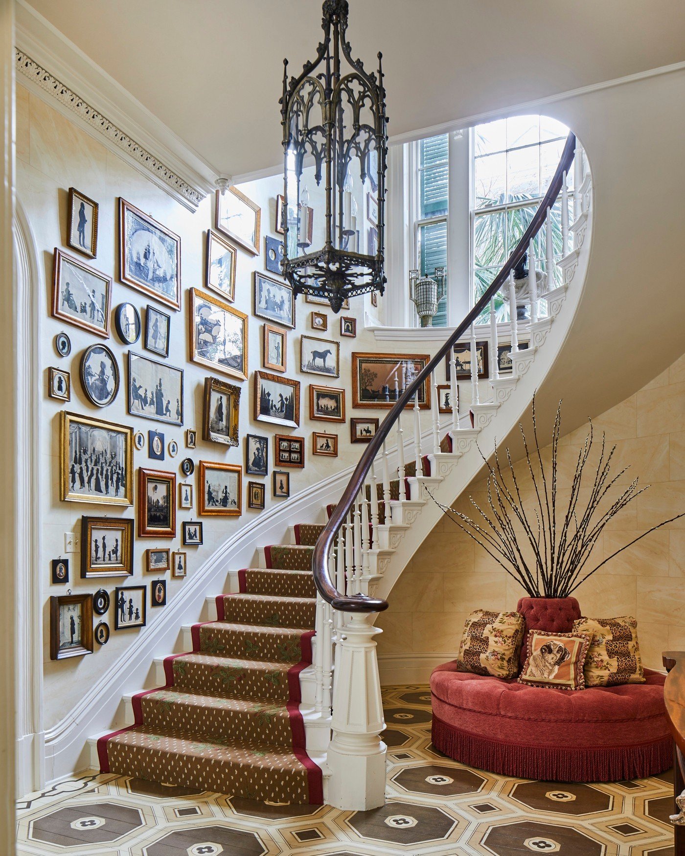 Curved staircase wall completely covered in framed vintage silhouette art and portraits in gold and wood frames.