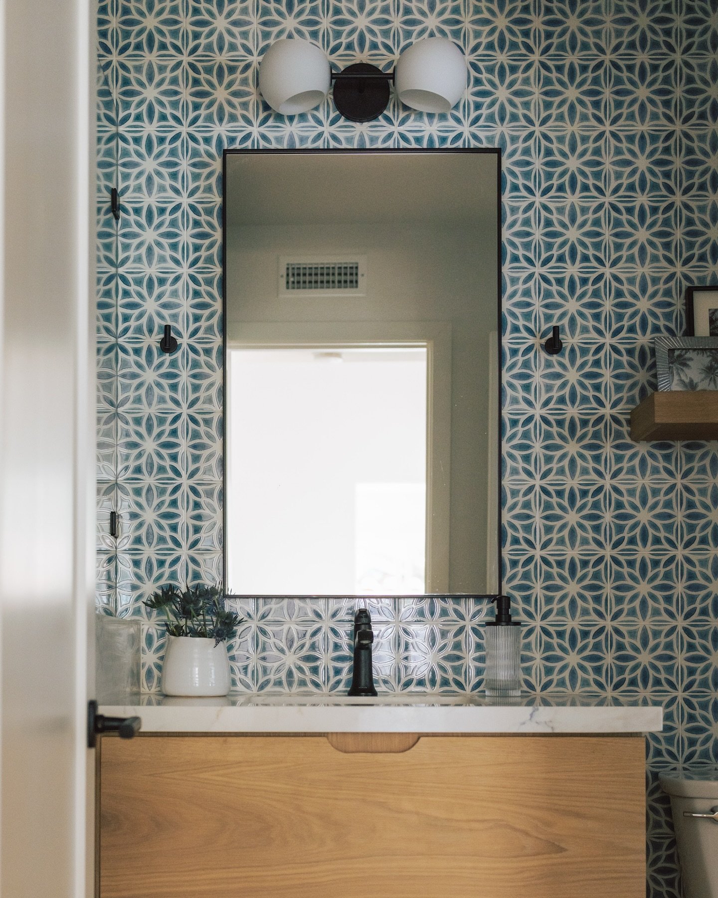 Bathroom vanity featuring a blue and white geometric tile accent wall with a wood cabinet.