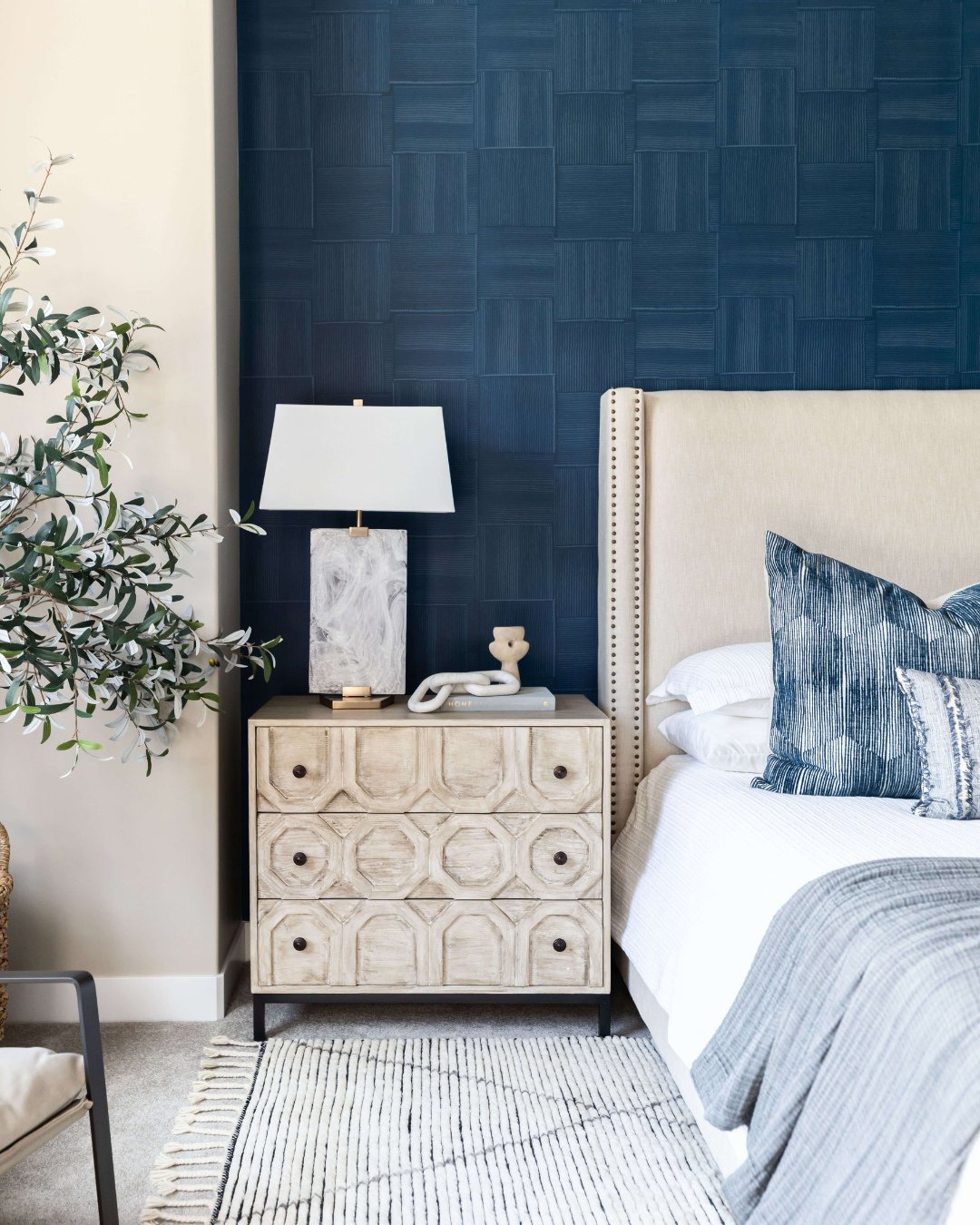 Navy blue accent wall featuring geometric woven square pattern behind beige upholstered bed