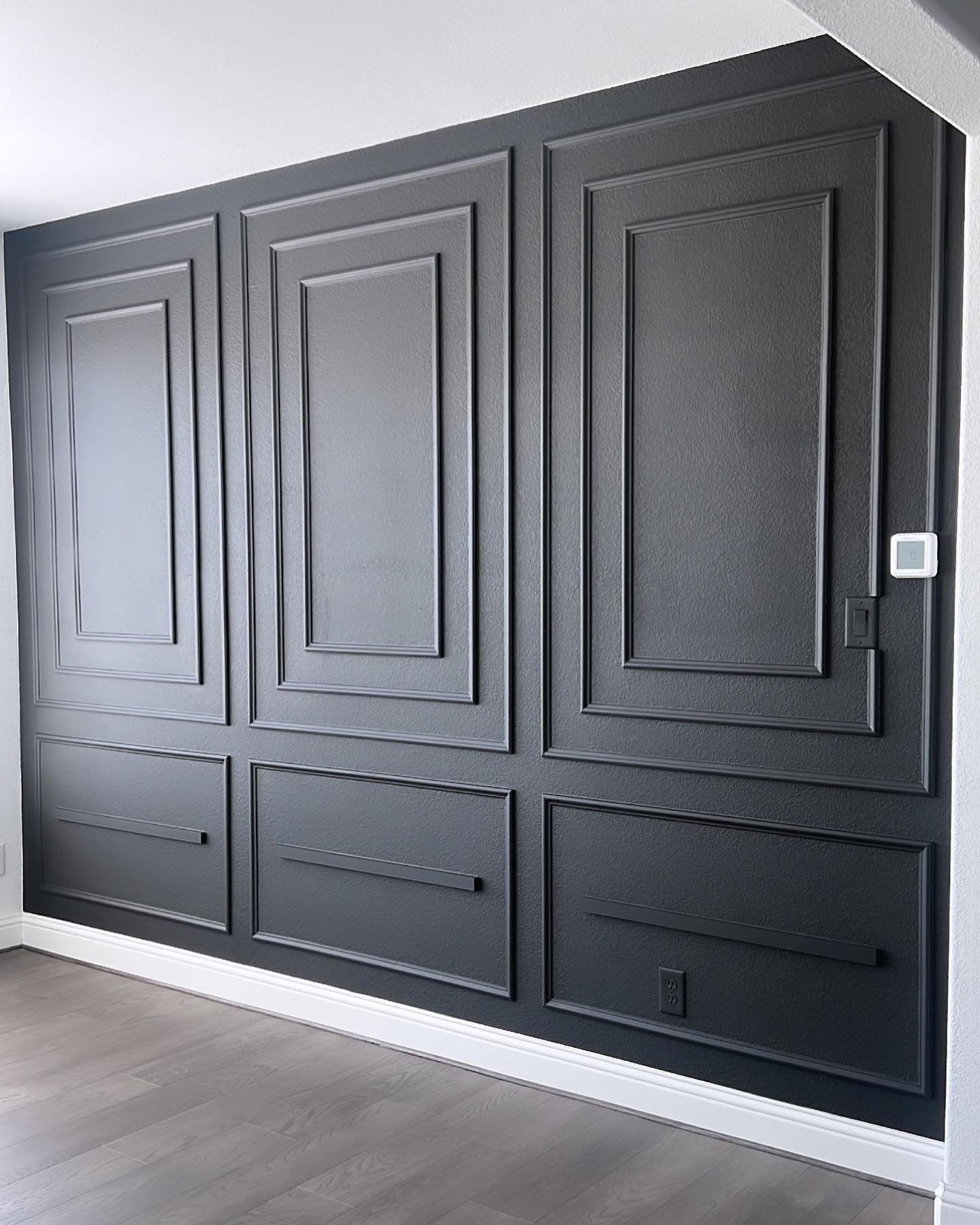 Black dining room accent wall featuring double picture frame molding and white baseboards.