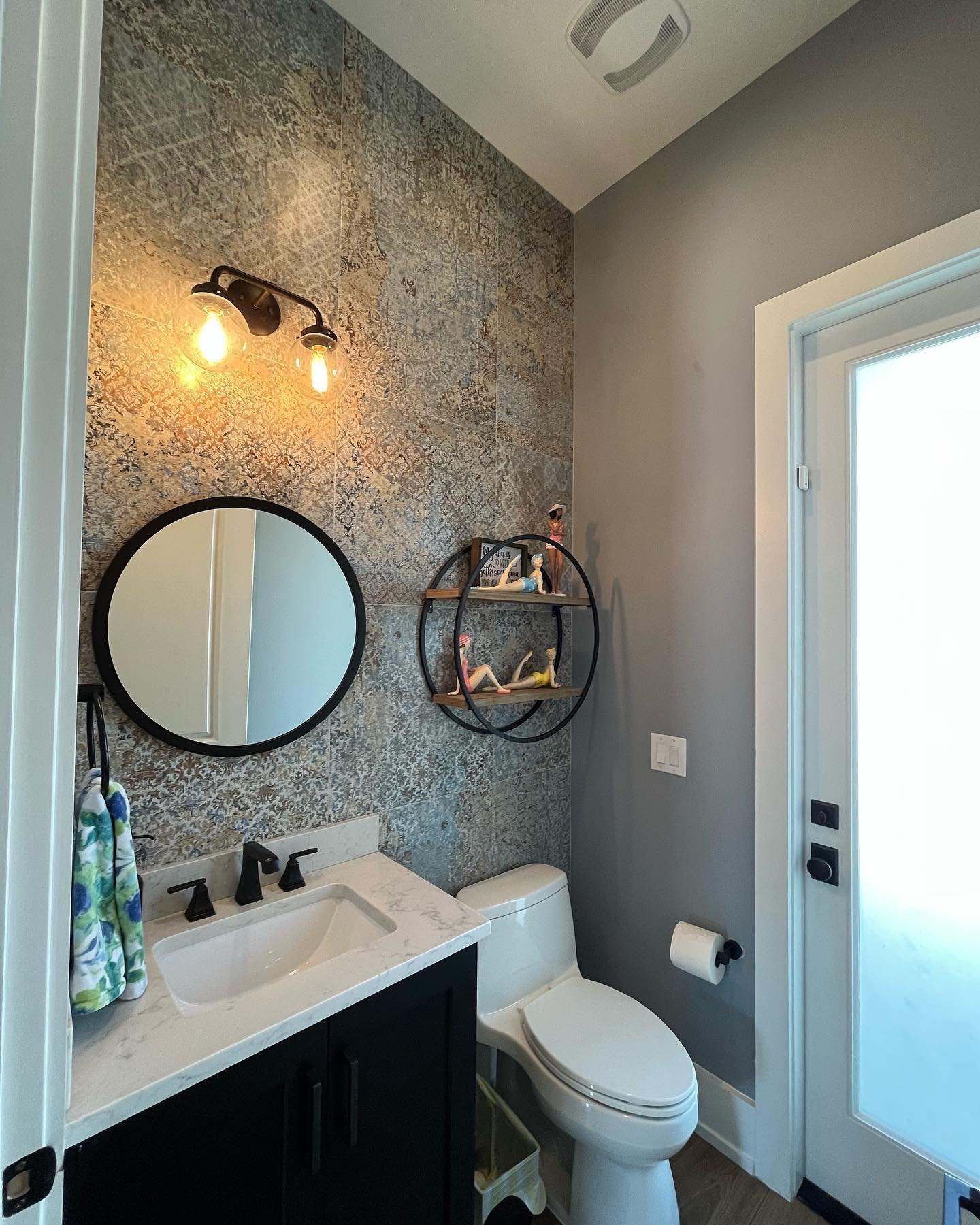 Bathroom accent wall with metallic patterned tiles and round black mirror