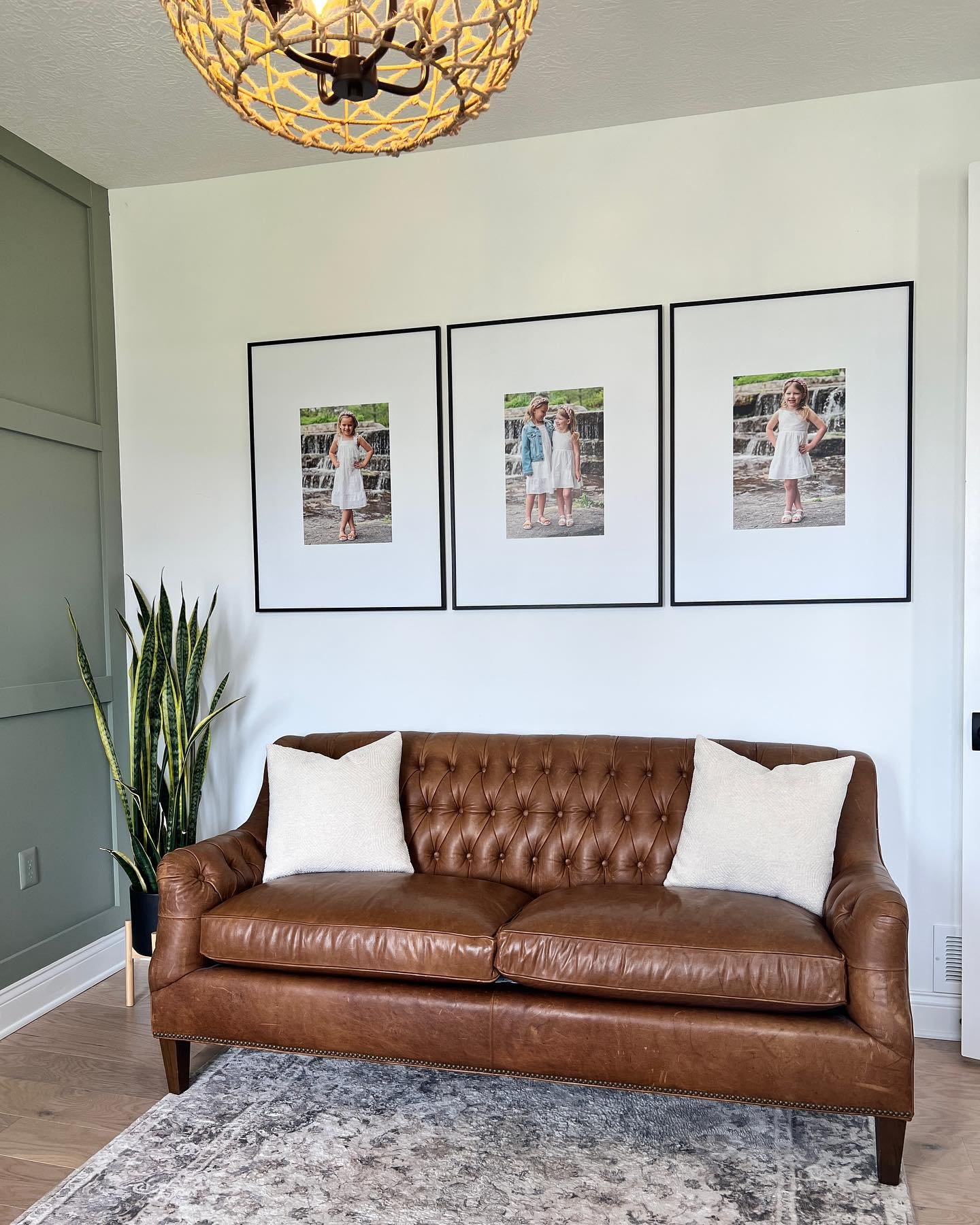 Three large black framed family portraits with wide white mats hanging above a leather couch.