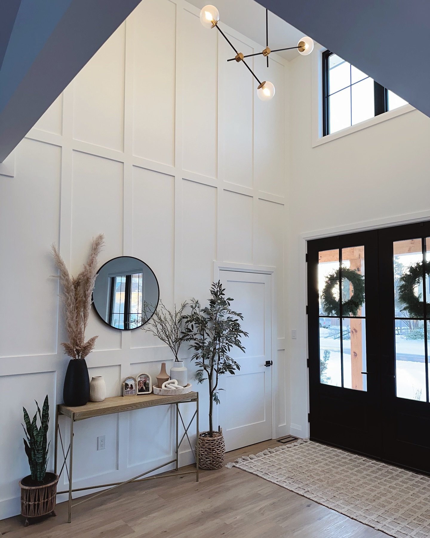 Tall entryway featuring white grid board and batten accent wall, double black doors, and modern chandelier.