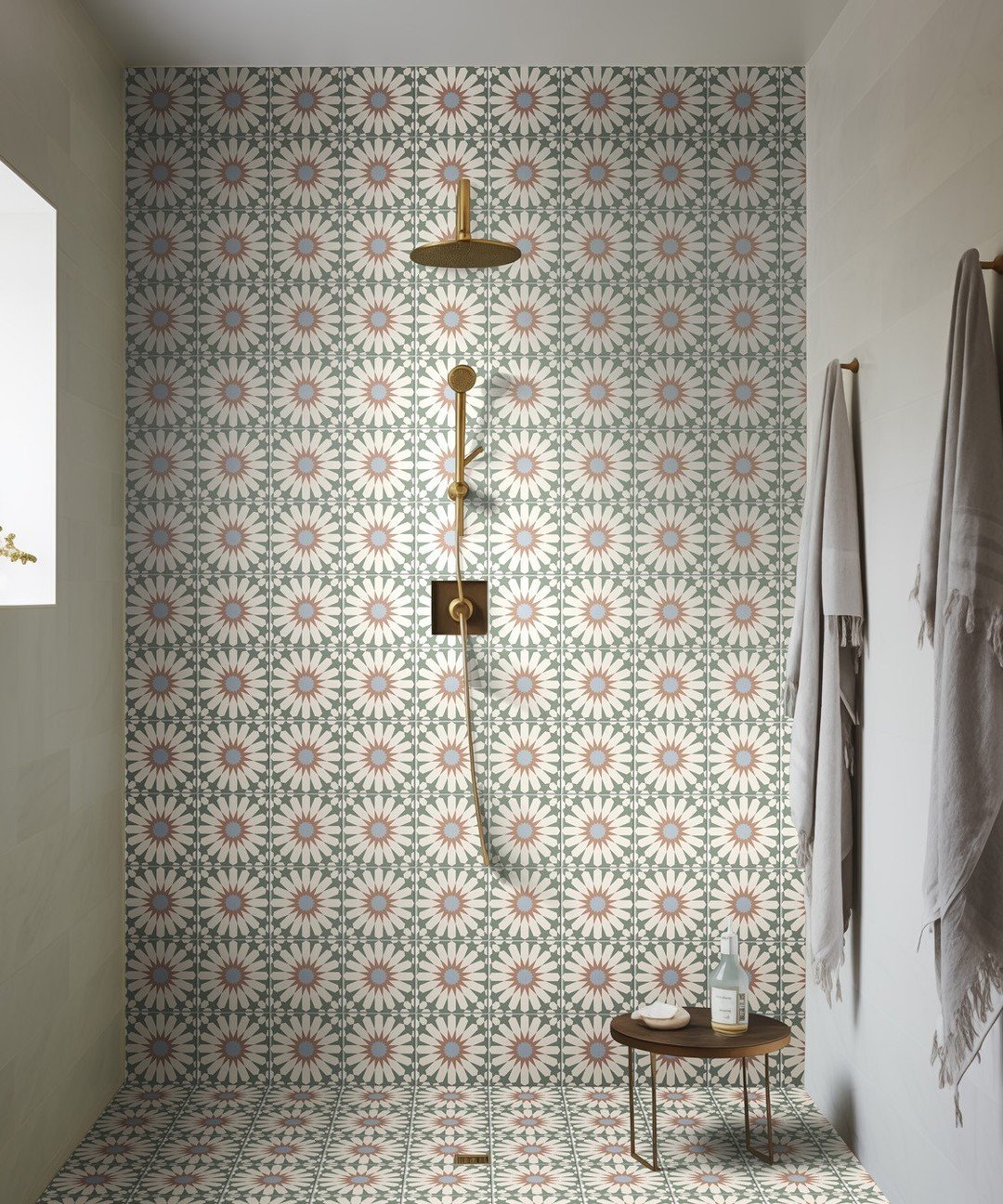 Shower area featuring green and pink daisy pattern tiles with gold fixtures.